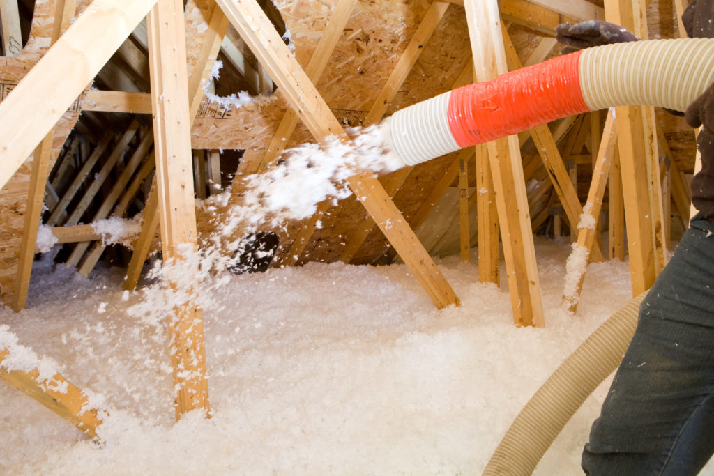 Worker Spraying Blown Fiberglass Insulation between Attic Trusses