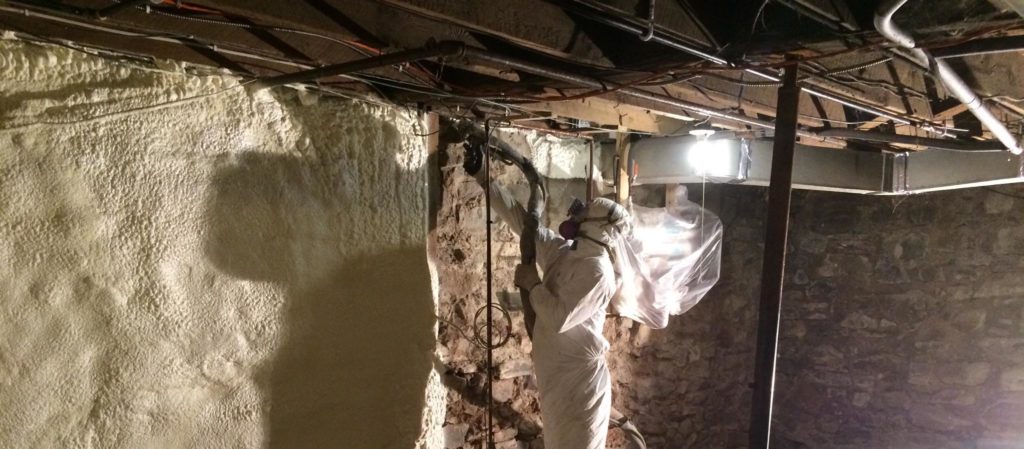man spraying foam insulation into crawlspace wall in basement of home