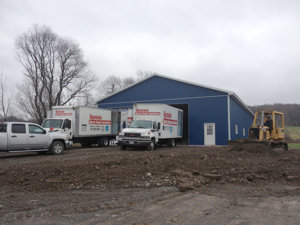 Blue pole barn being spray foamed with insulation from trailer